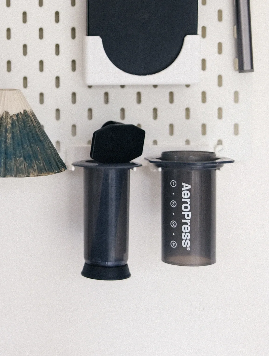 Aeropress parts drying on a minimal stand mounted to a white pegboard